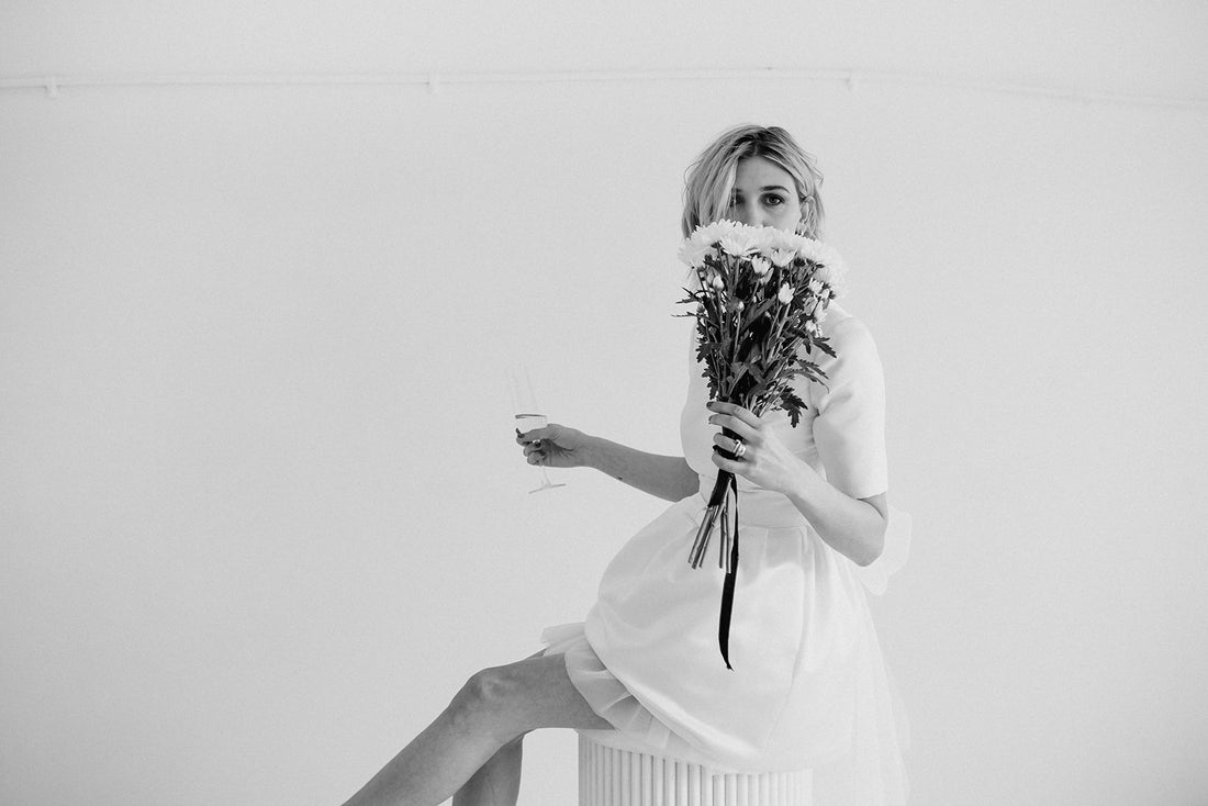 Black and white picture of model sitting holding a messy bunch of daisies in a short wedding dress